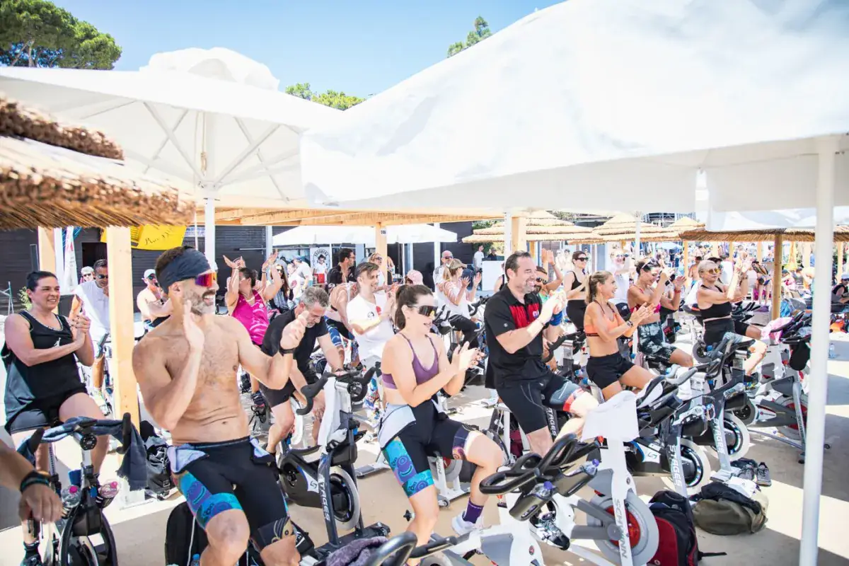 Riders cheering on Spinning® bikes under white seaside umbrellas